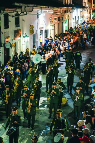 Colorful parade in Popayán, Cauca, Colombia, featuring marching band members playing instruments along a lively street.