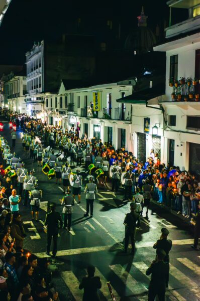 Crowds gather for a vibrant night parade in Popayán, Cauca, Colombia, with colorful costumes and lively street atmosphere.