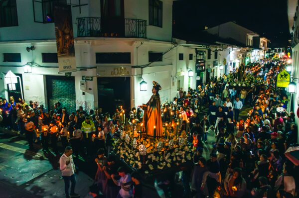 Lively procession with a statue surrounded by candlelight, filled with a crowd celebrating at night in Popayán, Cauca, Colombia.