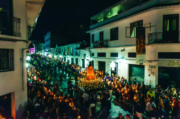 Crowds holding candles fill the streets of Popayán, Cauca, Colombia, illuminated by festive lights against the night sky.