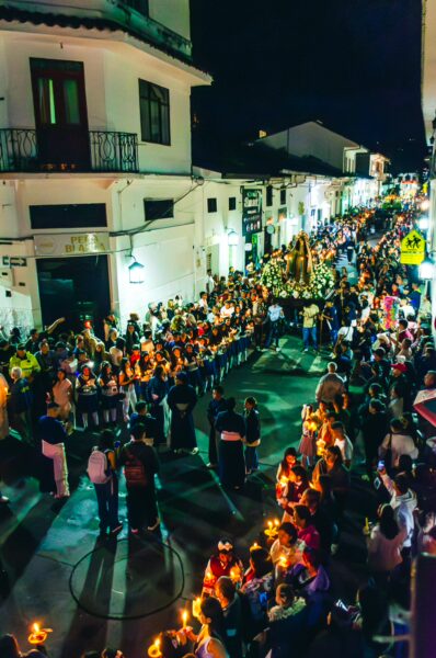 Crowds gather in Popayán, Cauca, Colombia, during a vibrant nighttime festival, illuminated by candles and street lights.