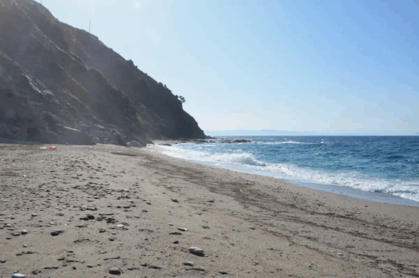 Clear blue waters meet golden sands at Kallianos Beach, framed by rocky cliffs under a bright blue sky.