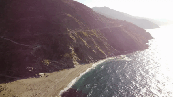 Golden sands meet shimmering waters at Kallianos Beach, surrounded by rugged cliffs and a scenic coastal road in Southern Evia.