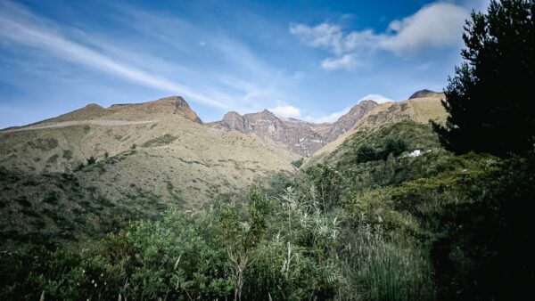 Lush green hills and rugged terrain frame the majestic Imbabura Volcano under a blue sky in Ecuador.