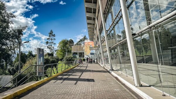 Lower cable car station at Pichincha Volcano features a modern structure with large windows, surrounded by green hills under a blue sky.