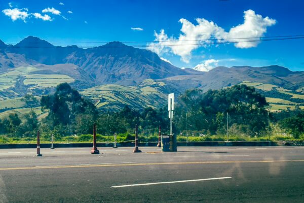 Lush green hills rise against a bright blue sky in Machachi, Ecuador, framed by distant mountains and a clear horizon.