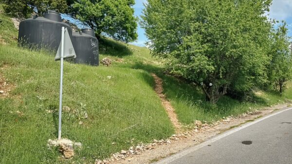 Dusty path leading up a grassy slope with small trees alongside the road in Magouliana to Valtesiniko, Arcadia, Greece.