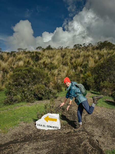 Volunteer on a hiking trail signpost with an arrow, surrounded by lush greenery and a dramatic sky in Ruminahui, Ecuador.