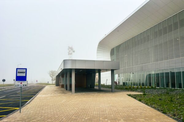 Modern airport architecture with sleek lines and foggy surroundings at Craiova, Romania, featuring a spacious entrance area and landscaping.