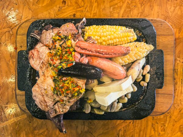 Sizzling mixed grill with meats, chorizo, and corn served on a wooden platter at La Ruta Restaurant, La Esperanza, Ibarra, Ecuador.