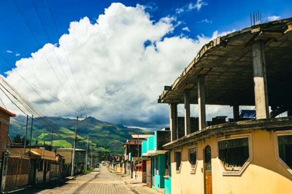 Vibrant street scene in Machachi, Ecuador, featuring colorful buildings and dramatic clouds over green mountains.