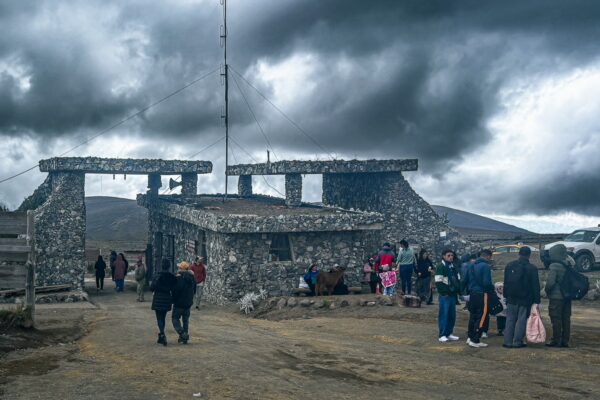 National park entrance with a stone structure, visitors gathered under a dramatic sky near Chimborazo Volcano, Ecuador.