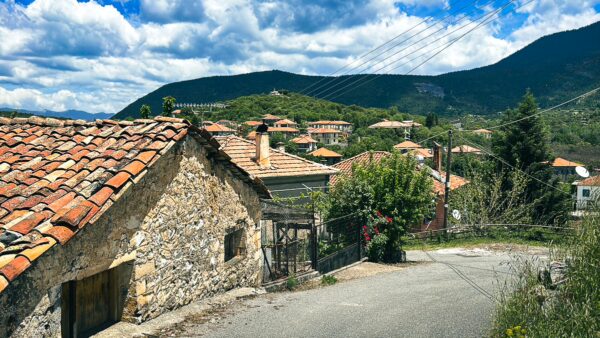 Charming stone houses with terracotta roofs line the winding road through Nymfasia, nestled in the lush hills of Arcadia, Greece.