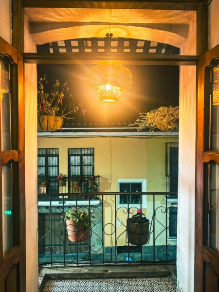 Cozy balcony view overlooking a colorful Quito street at night, illuminated by warm light and adorned with potted plants.