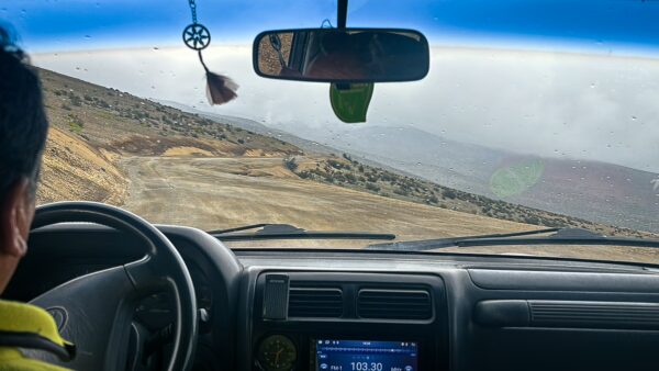 Chimborazo volcano looms in the distance, while a winding road leads through rugged terrain from a car’s interior view.