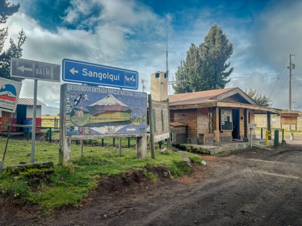 Rustic visitor center at Cotopaxi National Park in Ecuador, with directional signs and greenery in the background.