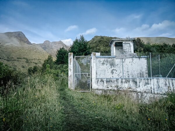 Abandoned structure surrounded by lush greenery and mountains near Imbabura Volcano in Ecuador, with a clear blue sky above.