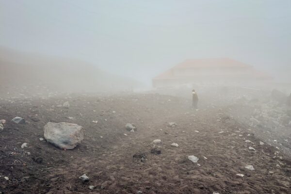 Fog envelops the rocky landscape of Mount Cotopaxi, with a distant figure walking towards the José Rivas Refuge, Ecuador.