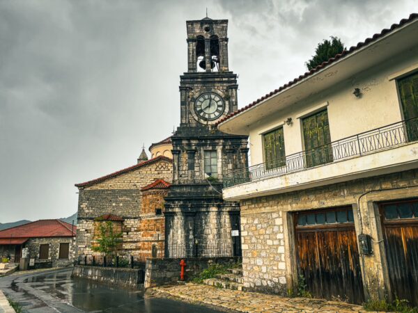 Historic clock tower stands prominently alongside stone buildings in Lagadia, Arcadia, Greece, under a moody sky.