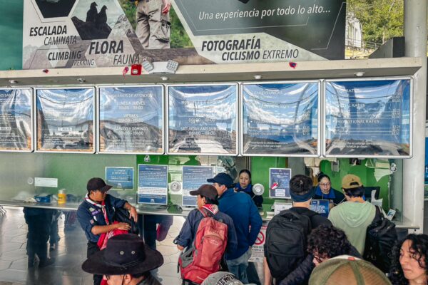 Lower cable car station at Pichincha Volcano in Ecuador, featuring visitors and ticket counters under informative displays.