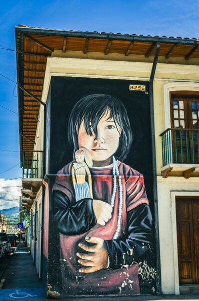 Vibrant mural featuring a child holding a bird on a historic building in Machachi, Ecuador, set against a bright blue sky.
