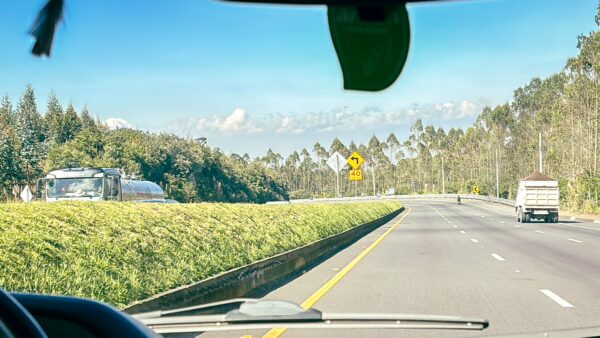Scenic view along the highway in Machachi, Ecuador, featuring lush green fields and trees under a clear blue sky.