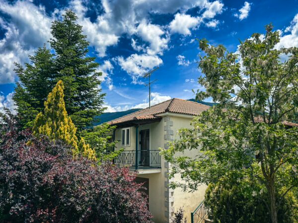 Charming stone house with a terracotta roof surrounded by vibrant greenery and dramatic clouds in Nymfasia, Arcadia, Greece.