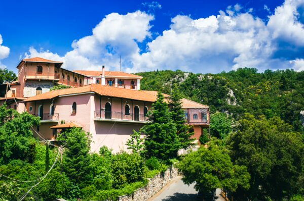 Panagia Kernitsis Monastery features pink buildings nestled among green trees, set against a backdrop of blue skies in Arcadia, Greece.