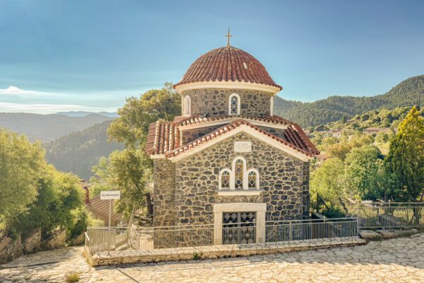 Charming stone church with a red-tiled roof nestled in the hills of Lagadia, Arcadia, Greece, surrounded by lush greenery.