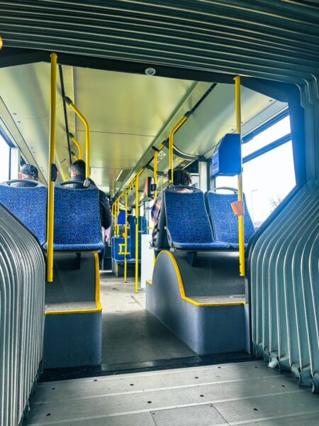 Interior view of an airport bus in Craiova, Romania, featuring blue seats, yellow poles, and passengers seated near the windows.