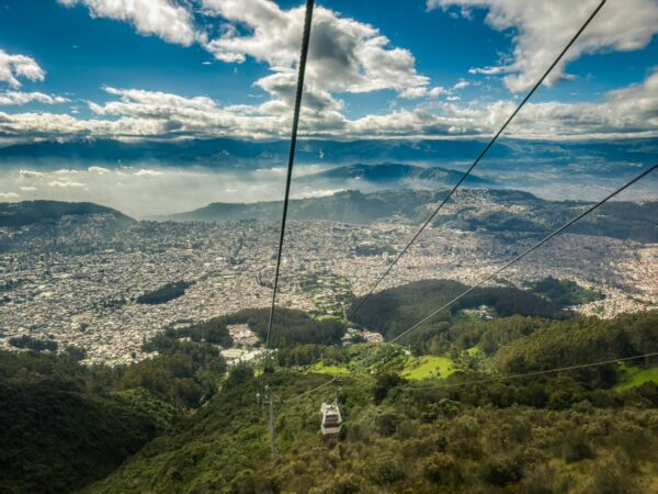 Cable car gliding over lush hills and the sprawling city views of Quito, with Pichincha Volcano in the background, Ecuador.