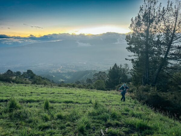 Sunset view from Imbabura Volcano, Ecuador, showcasing lush green grass and a distant cityscape under a colorful sky.