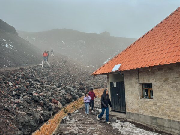 Hikers navigate the rocky terrain near the José Rivas Refuge, surrounded by misty views of Mount Cotopaxi, Ecuador.