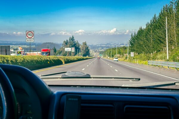 Clear highway stretches towards snow-capped peaks in Chimborazo, Ecuador, framed by lush greenery and blue skies.