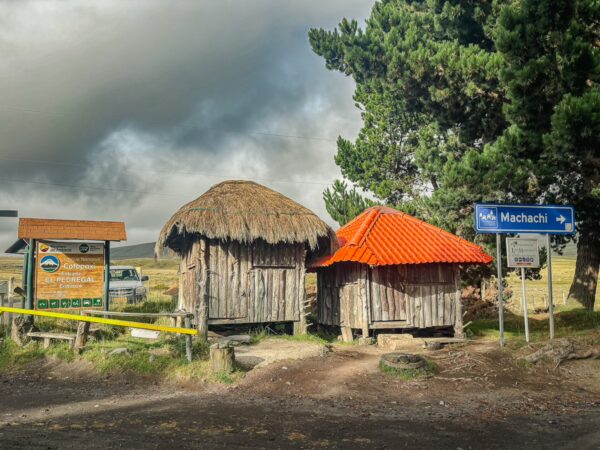 Traditional thatched huts at the north entrance of Cotopaxi National Park, framed by lush greenery and dramatic skies in Ecuador.