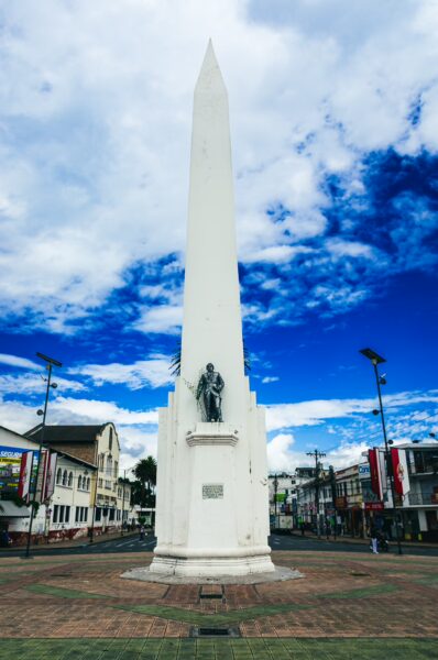 Obelisco de la Estación stands tall against a vibrant blue sky, surrounded by colorful buildings in Ibarra, Ecuador.