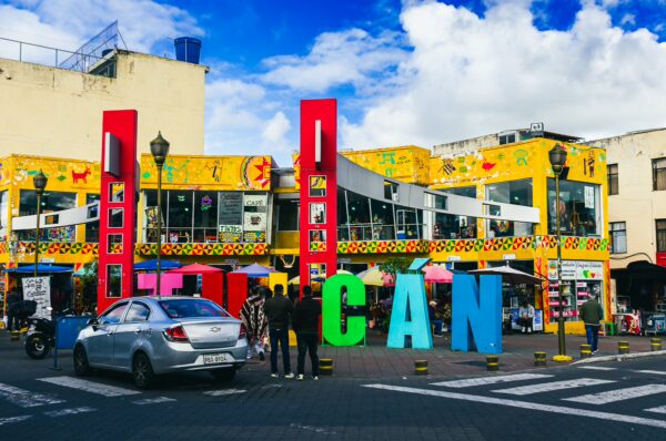 Colorful buildings adorned with vibrant murals and a large "TULCÁN" sign in a bustling area of Tulcán, Ecuador.