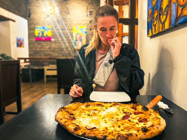 Enjoying a large pepperoni pizza at Bocanada, a cozy restaurant in Quito, Ecuador, with colorful artwork in the background.