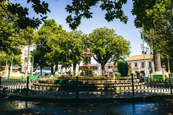 Central Park features a decorative fountain surrounded by lush trees and vibrant greenery in Machachi, Ecuador.