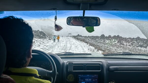 Snow-covered road leads to Chimborazo Volcano in Ecuador, with a person driving and scenic mountains visible through the windshield.