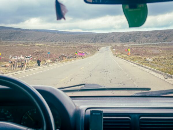 Scenic view from a vehicle's dashboard along the road to Chimborazo, Ecuador, with rugged landscapes and distant hills.