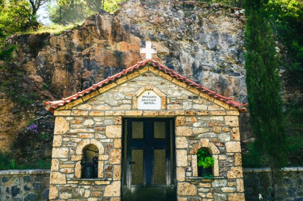 Panagia Kernitsis Monastery features a stone facade with a red-tiled roof, surrounded by lush greenery in Arcadia, Greece.