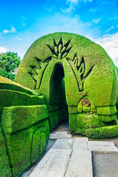 Intricate hedges create archway formations at Tulcán Cemetery in Ecuador, under a bright blue sky with lush greenery.