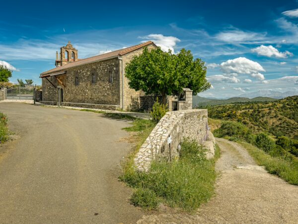Quaint stone church surrounded by lush greenery and rolling hills in Vytina, near Nymfasia, Arcadia, Greece under a clear blue sky.