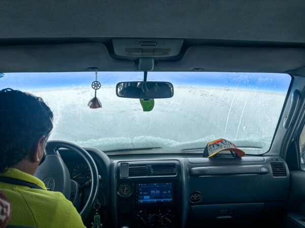Driving towards Chimborazo Volcano, the view through a car windshield shows a misty landscape and a distant, snowy peak in Ecuador.