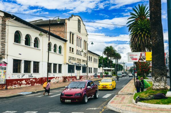 Colorful streets of Ibarra, Ecuador, featuring vintage architecture, palm trees, and bustling traffic with red and yellow cars.
