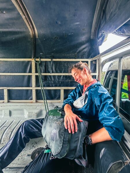 Traveler in a blue rain jacket resting inside a vehicle with a backpack, surrounded by a rugged, earthy interior in Ibarra, Ecuador.