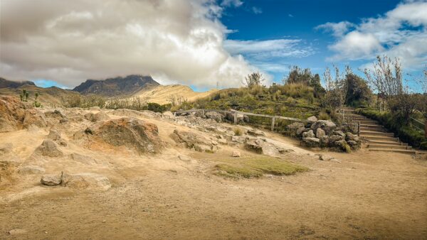 Pichincha Volcano in Ecuador showcases a rugged landscape with dry terrain, distant peaks, and a vibrant blue sky.
