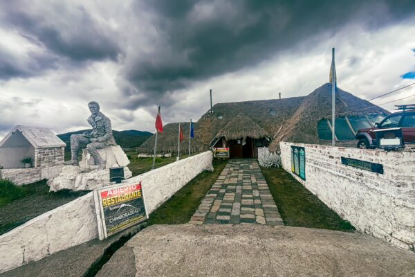 Rey Venture restaurant lodge features a stone path leading to a thatched-roof building under a dramatic sky in Machachi, Ecuador.
