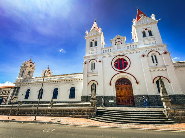 Elaborate white church features red accents and pointed towers against a blue sky in Machachi, Ecuador.